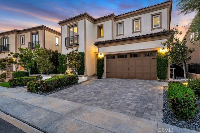 mediterranean / spanish house featuring stucco siding, decorative driveway, an attached garage, and a tiled roof