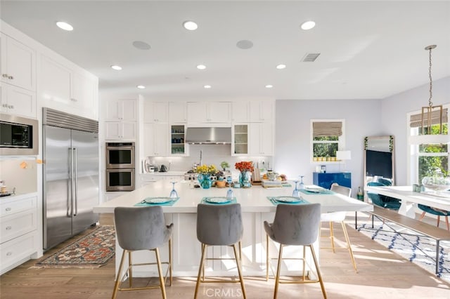 kitchen featuring built in appliances, under cabinet range hood, light wood-style flooring, tasteful backsplash, and a kitchen island