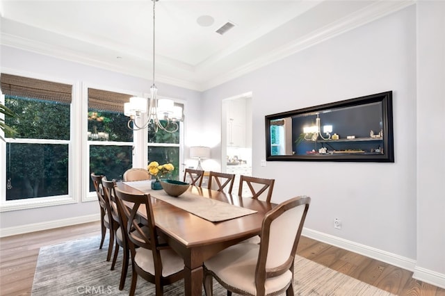 dining area featuring wood finished floors, a chandelier, baseboards, a raised ceiling, and crown molding