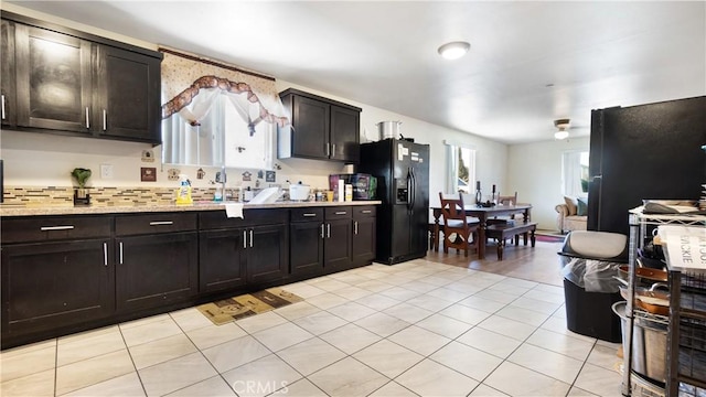 kitchen featuring black fridge, light tile patterned floors, backsplash, and light stone counters
