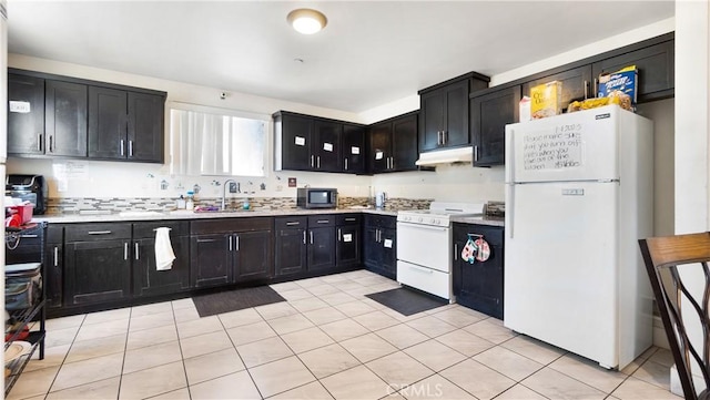 kitchen with white appliances, under cabinet range hood, dark cabinets, and a sink