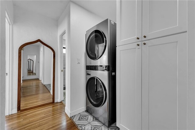 washroom featuring stacked washer / dryer, light wood-style floors, and baseboards