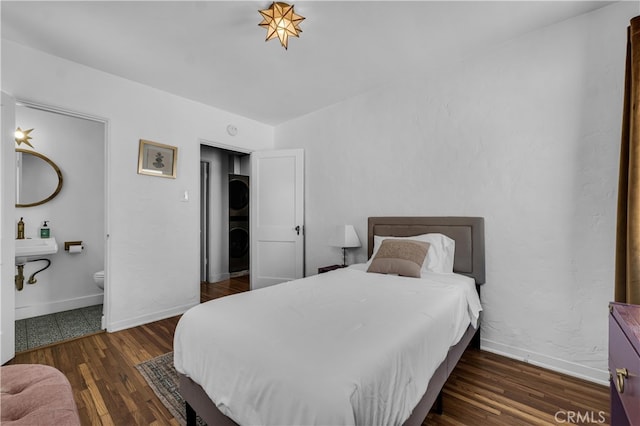 bedroom with estacked washer and dryer, wood finished floors, ensuite bath, and baseboards