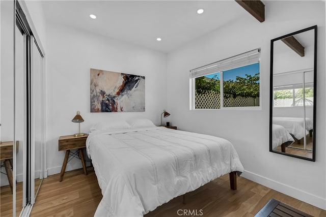 bedroom featuring wood finished floors, beamed ceiling, baseboards, recessed lighting, and a closet