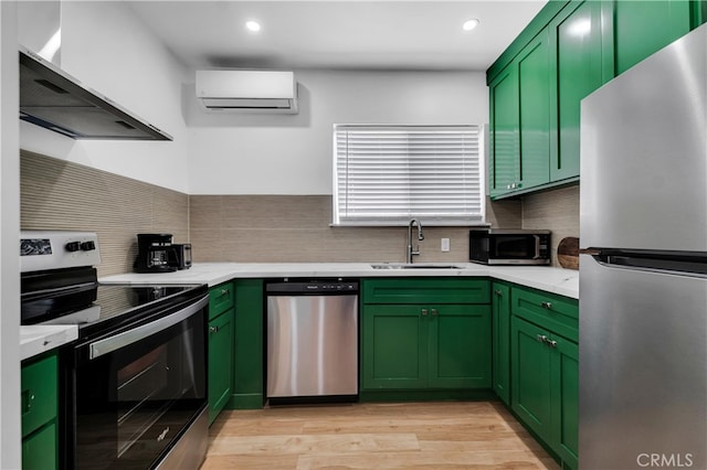 kitchen featuring stainless steel appliances, green cabinetry, a sink, an AC wall unit, and wall chimney range hood