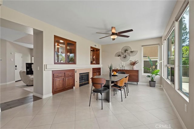 dining space featuring a glass covered fireplace, light tile patterned floors, ceiling fan, and baseboards