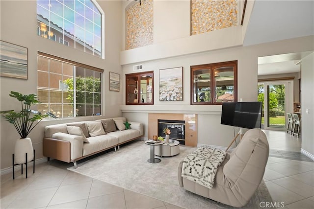 tiled living room with a towering ceiling, baseboards, and a tile fireplace