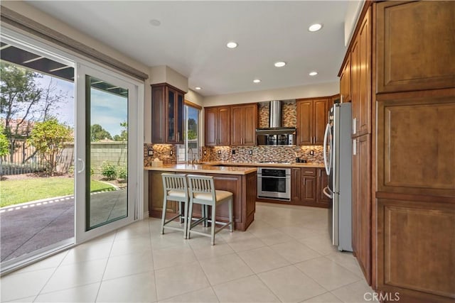 kitchen featuring appliances with stainless steel finishes, wall chimney exhaust hood, a peninsula, light countertops, and decorative backsplash