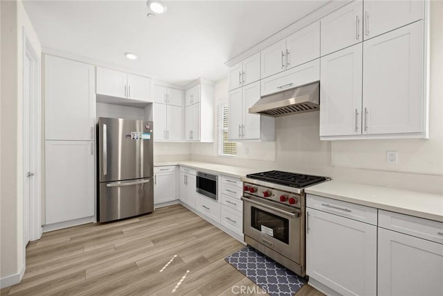 kitchen featuring stainless steel appliances, under cabinet range hood, white cabinets, light wood-style flooring, and light countertops