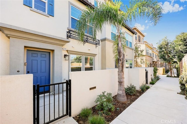 view of exterior entry featuring stucco siding, fence, a gate, and a residential view