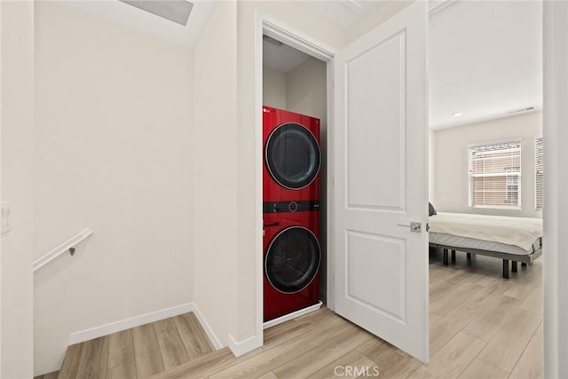 laundry area featuring estacked washer and dryer, light wood finished floors, and baseboards
