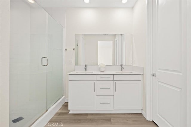 full bathroom with a stall shower, wood finished floors, double vanity, and recessed lighting