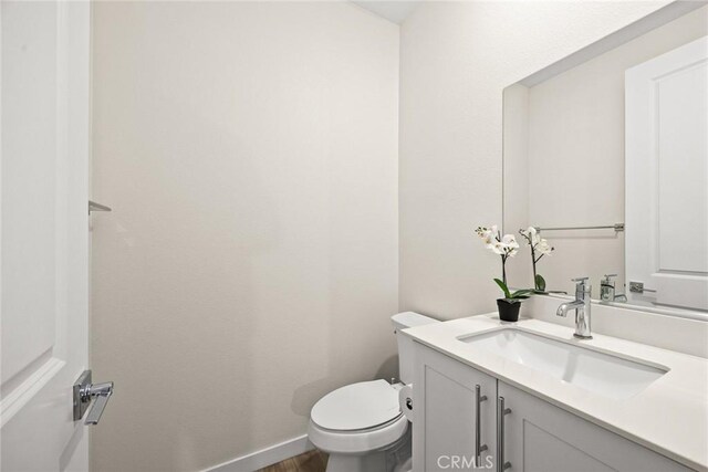 half bath featuring vanity, toilet, baseboards, and wood finished floors
