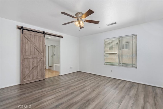 empty room featuring a barn door, light wood finished floors, a ceiling fan, and baseboards