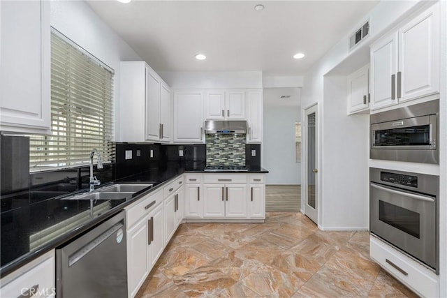 kitchen with appliances with stainless steel finishes, a sink, white cabinetry, decorative backsplash, and under cabinet range hood