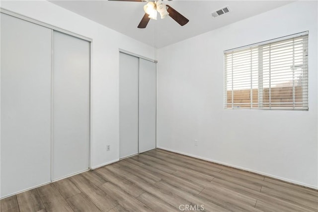 unfurnished bedroom featuring wood finished floors, multiple closets, a ceiling fan, and baseboards