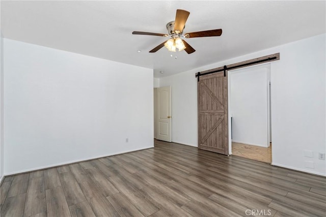 unfurnished bedroom featuring wood finished floors, a barn door, baseboards, and ceiling fan