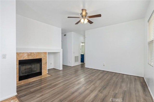 unfurnished living room with a ceiling fan, wood finished floors, a tiled fireplace, and baseboards