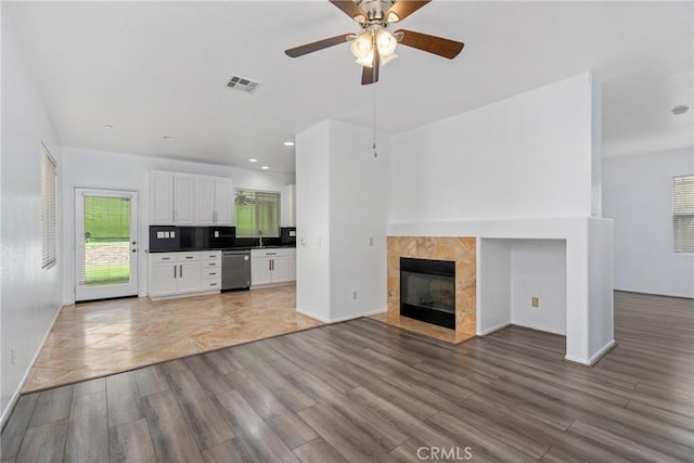 unfurnished living room with light wood-type flooring, ceiling fan, baseboards, a sink, and a tiled fireplace