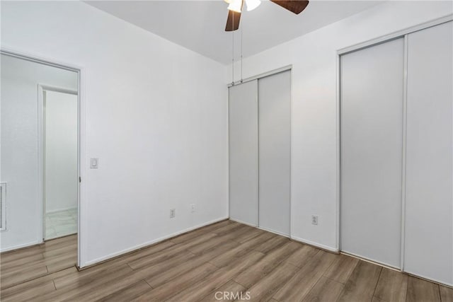 unfurnished bedroom featuring wood finished floors, multiple closets, and a ceiling fan