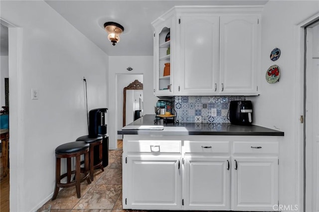 kitchen with backsplash, white cabinetry, dark countertops, glass insert cabinets, and baseboards