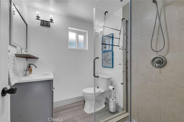 bathroom with a stall shower, toilet, wood finished floors, and vanity