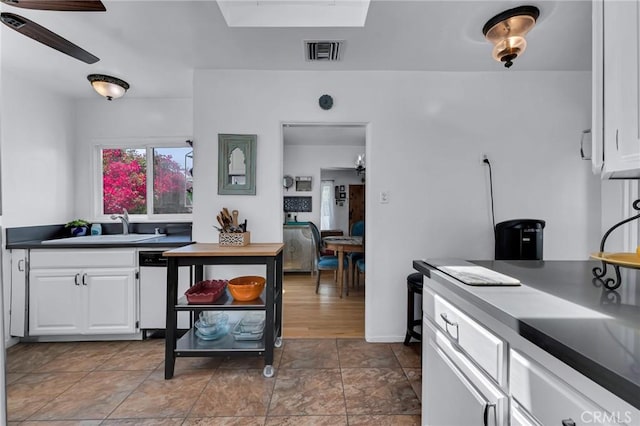 kitchen featuring white cabinetry, a sink, white dishwasher, ceiling fan, and dark countertops