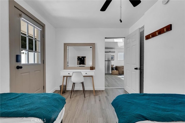 bedroom with freestanding refrigerator, wood finished floors, baseboards, a wall mounted air conditioner, and a ceiling fan