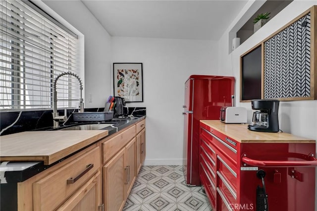 kitchen featuring butcher block counters, a sink, freestanding refrigerator, and light floors