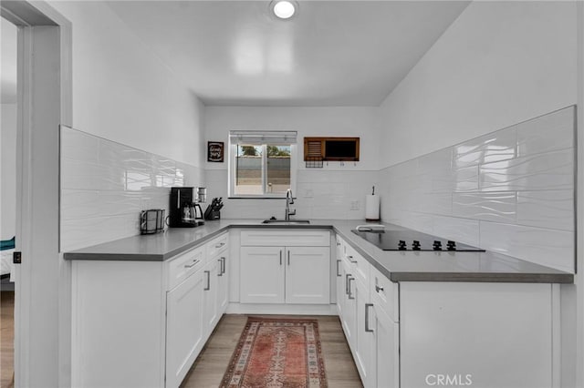 kitchen featuring black electric stovetop, a sink, wood finished floors, tasteful backsplash, and white cabinets