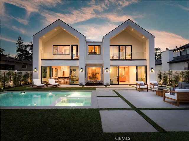 back of property at dusk featuring a balcony, an outdoor hangout area, a patio, stucco siding, and fence