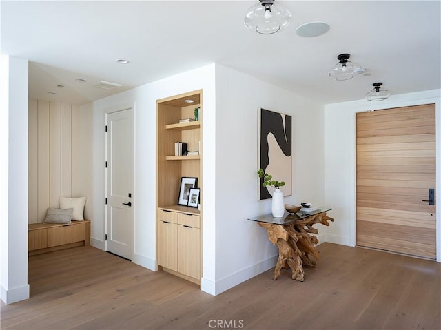 hallway featuring light wood-type flooring, baseboards, and built in shelves