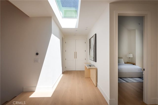 hall with light wood finished floors, a skylight, and baseboards