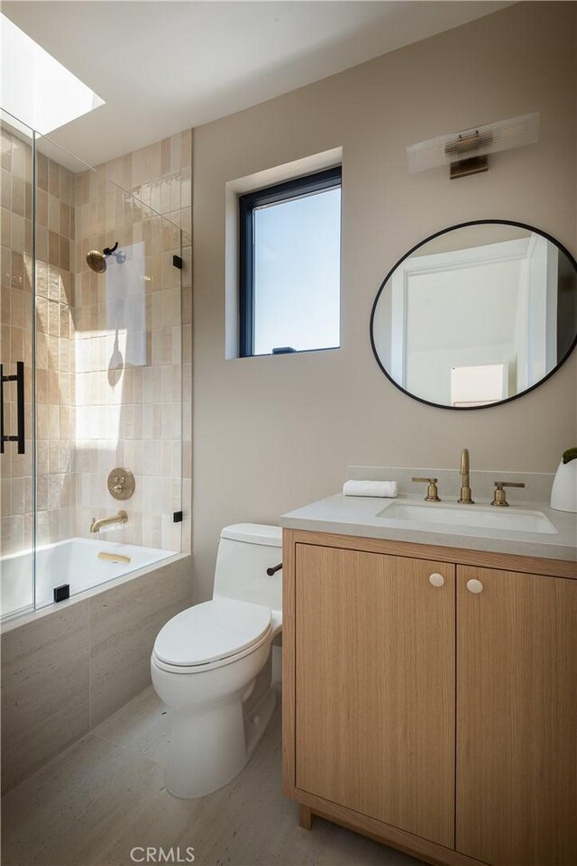 bathroom featuring tiled shower / bath, toilet, vanity, and a skylight