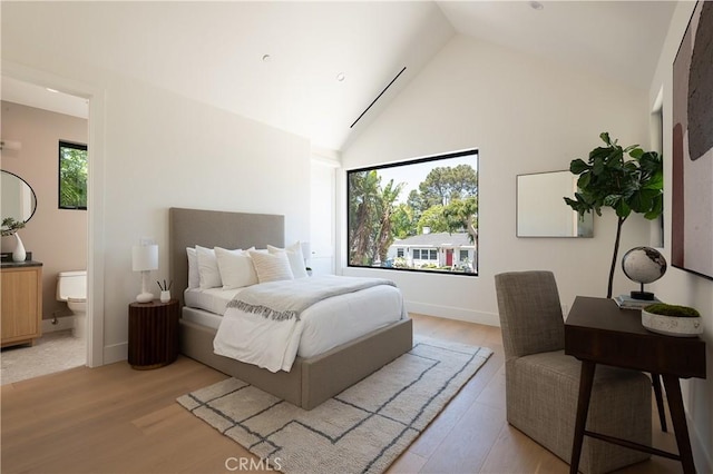 bedroom featuring multiple windows, high vaulted ceiling, light wood finished floors, ensuite bath, and baseboards