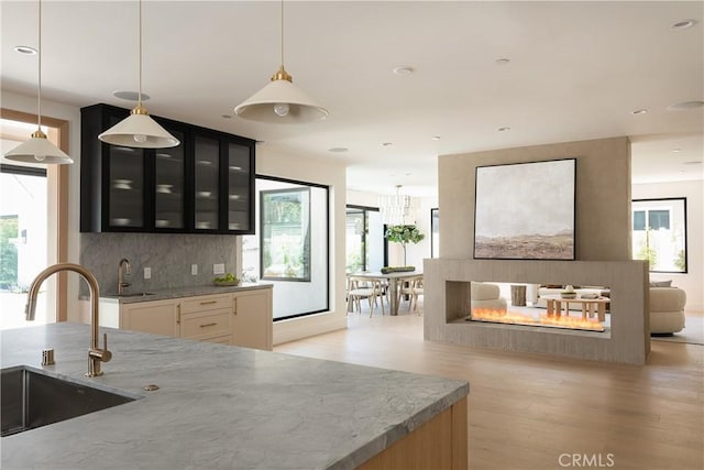 kitchen with a sink, light stone counters, light wood-style flooring, glass insert cabinets, and dark cabinets