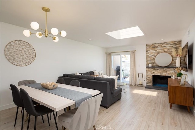 dining space with light wood-style floors, a skylight, a chandelier, and a stone fireplace