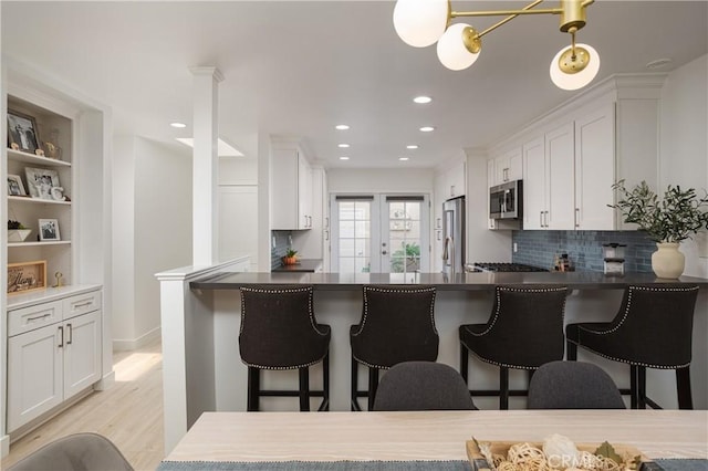 kitchen with appliances with stainless steel finishes, tasteful backsplash, white cabinets, light wood-style flooring, and a kitchen breakfast bar