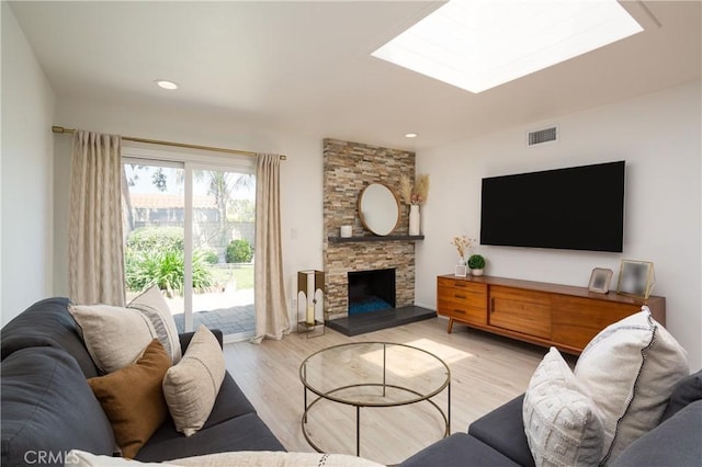 living area featuring light wood-style flooring, a fireplace, a skylight, and recessed lighting