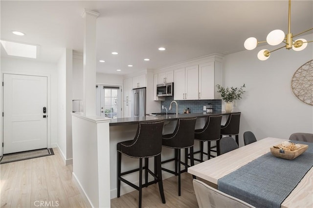 kitchen featuring stainless steel appliances, decorative backsplash, white cabinetry, a peninsula, and light wood-style floors