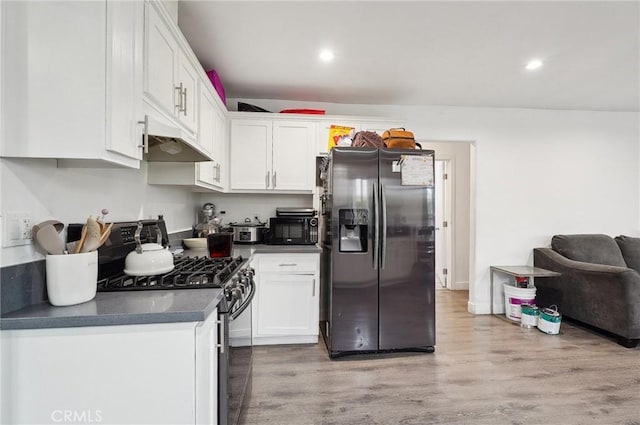 kitchen featuring black appliances, under cabinet range hood, white cabinetry, light wood-type flooring, and dark countertops