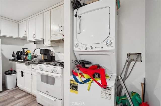 kitchen with white gas range, stacked washer and clothes dryer, white cabinets, light wood-style floors, and under cabinet range hood