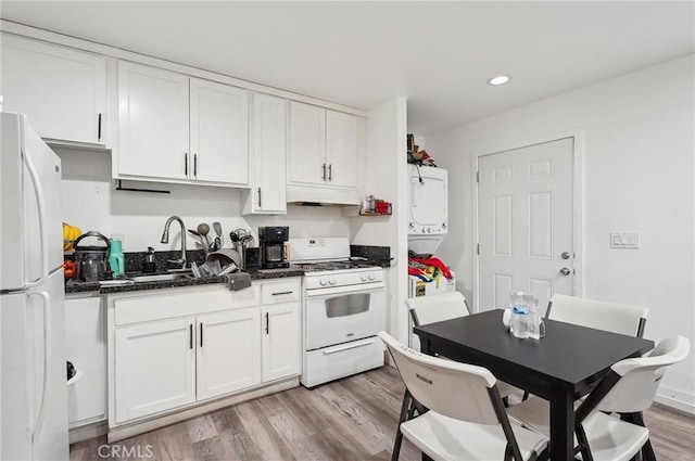 kitchen featuring white appliances, estacked washer and dryer, a sink, under cabinet range hood, and white cabinets