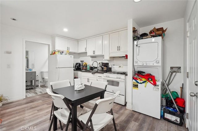 kitchen featuring white appliances, stacked washing machine and dryer, light wood-type flooring, white cabinets, and recessed lighting