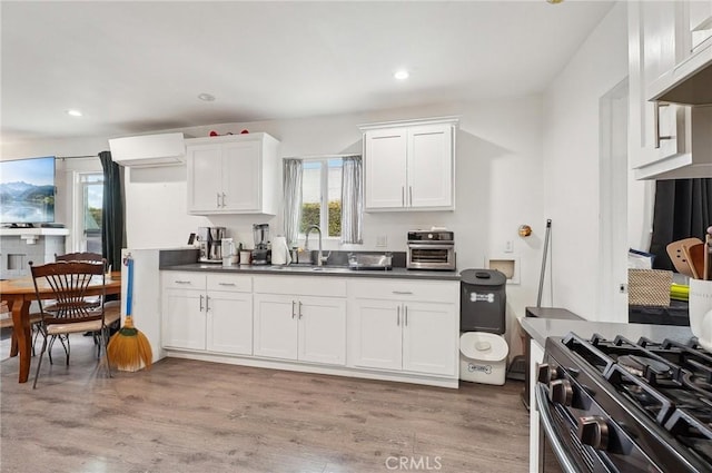 kitchen with a sink, white cabinets, gas range oven, light wood-style floors, and recessed lighting