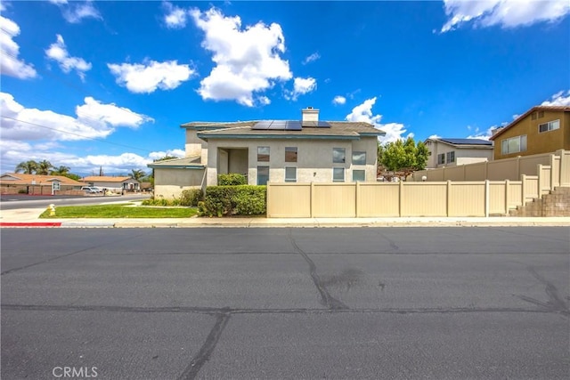 view of front of property with roof mounted solar panels, fence, a chimney, and stucco siding
