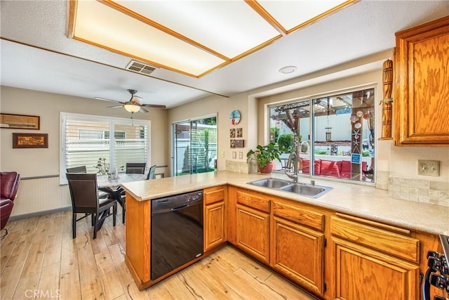 kitchen featuring dishwasher, a sink, light countertops, a peninsula, and brown cabinetry