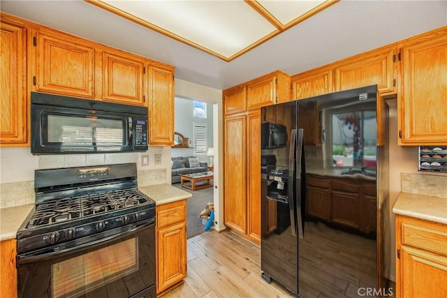 kitchen featuring black appliances, light countertops, light wood-style floors, and brown cabinetry