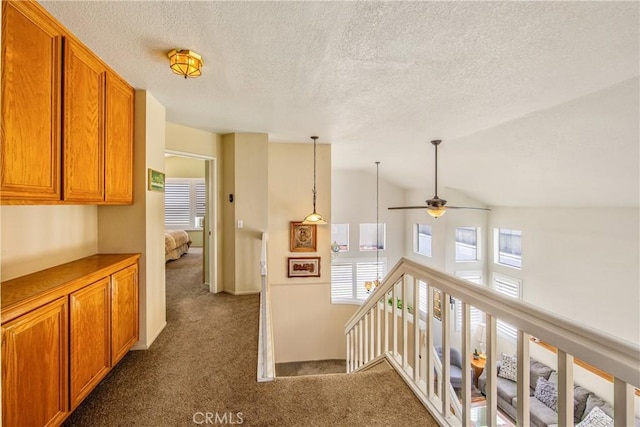 hall with dark colored carpet, plenty of natural light, an upstairs landing, and a textured ceiling