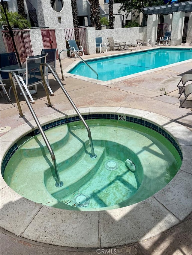 community pool featuring fence, a patio area, and a hot tub